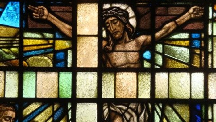 Das Glasfenster zeigt Jesus am Kreuz mit zwei Gestalten darunter