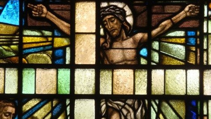 Das Glasfenster zeigt Jesus am Kreuz mit zwei Gestalten darunter