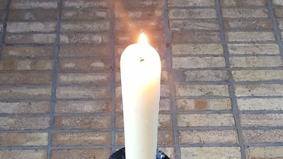 Eine Kerze steht auf einem Ziegelboden in einem Halter.