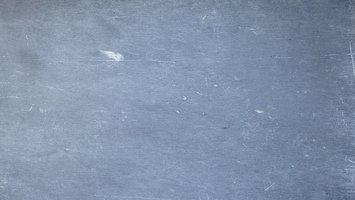 Eine Nahaufnahme einer abgenutzten, grauen Tafel mit verblassten Markierungen und leichten Oberflächenkratzern.