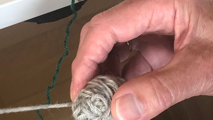 Hånd holder en lille ballede guldgul tråd og en lang grøn tråd.