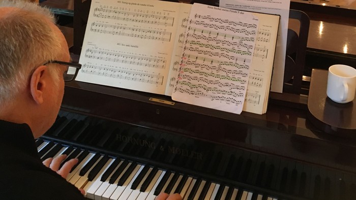 En mand spiller piano med noter og en lygt på instrumentet