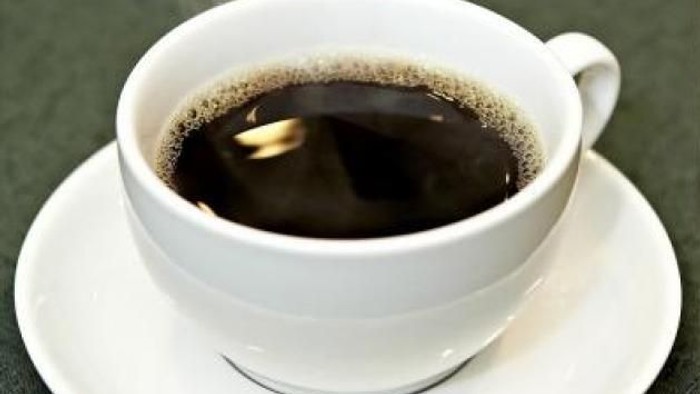 En hvid tekop i en kop og skål med mørk kaffe og skum.