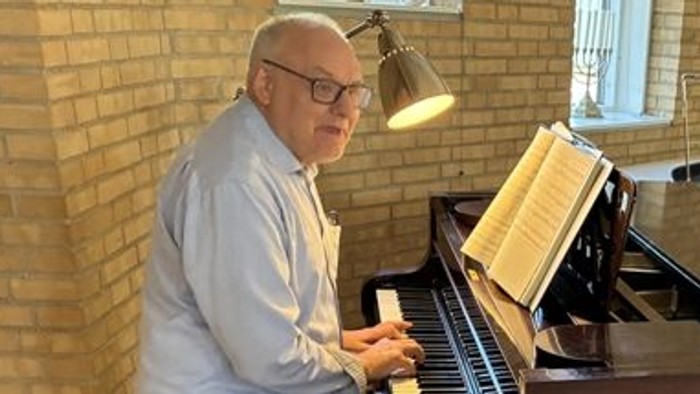 Manden spiller klaver, mens kvinden iagttager, begge smiler.