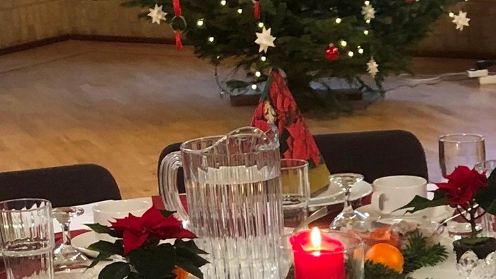 En festligt jul-bord med julerose, lyse, og pyntet juletree i baggrunden