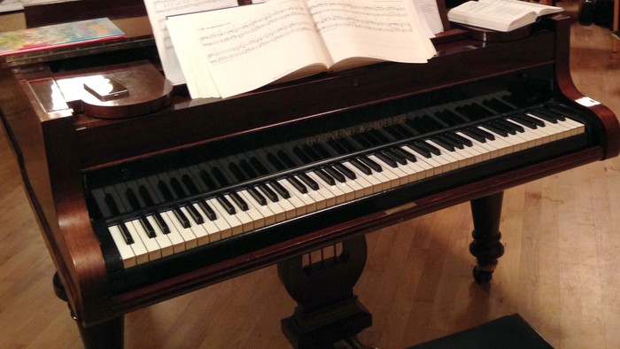 En gruppe af mennesker sidder i en seng og ser en pianotilstelning.