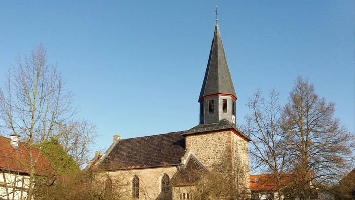Kirche mit hohem Kirchturm und umgebenden Bäumen.