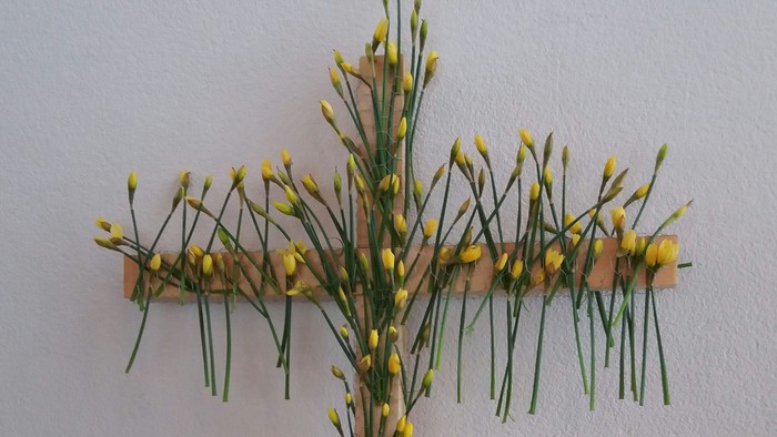 Eine kreuzförmige Anordnung aus gelben Blüten und grünen Stängeln an einer Wand.