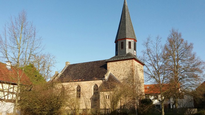 Kirche mit hohem Kirchturm und umgebenden Bäumen.