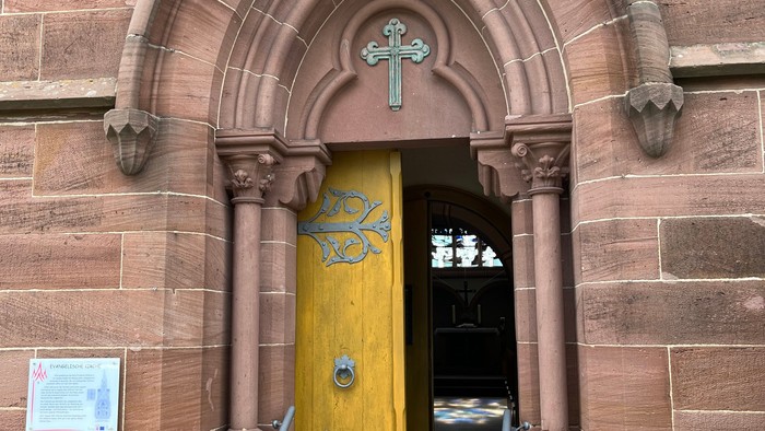 Kircheneingang mit bogigem Türbogen und gelber Tür.