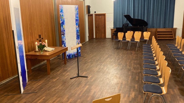 Ein geräumiger Raum mit Holzbestuhlung für eine Veranstaltung, ausgestattet mit einem dekorierten Altar und einer Bühnenrückwand.
