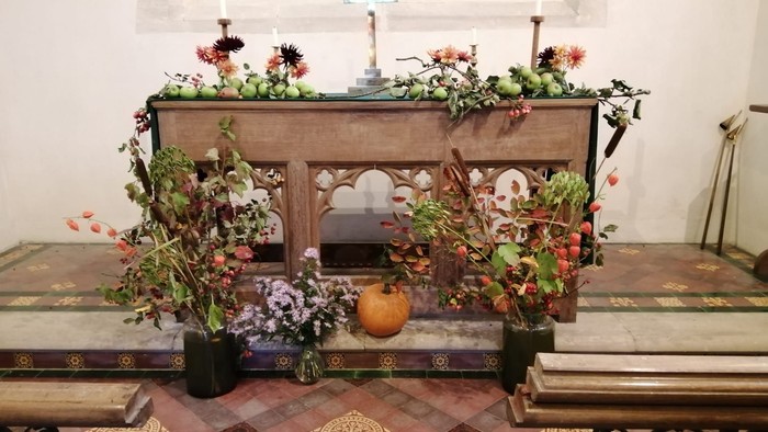 Altar decorated with flowers, candles, and pumpkin.