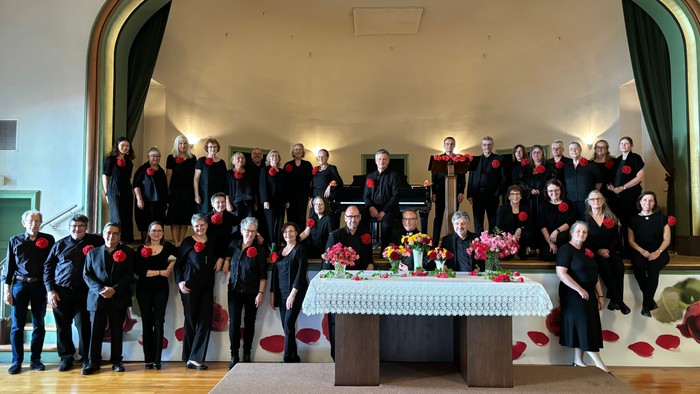 Ein großer Chor posiert vor einem Tisch mit Blumenarrangements in einem Saal