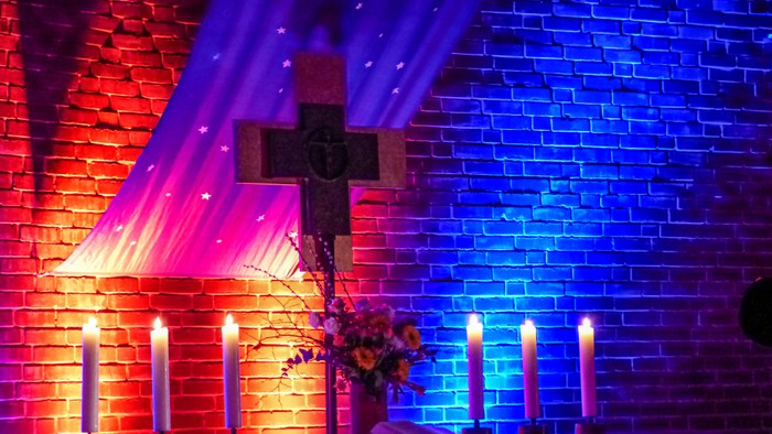 Kirchenaltar mit Kreuz und Kerzen, beleuchtet mit bunten Lichtern