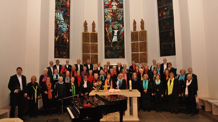 Eine Gruppe von Menschen posiert in einer Kirche vor einem Altar und buntem Kirchenfenster