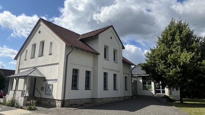 Das Bild zeigt das Laggenbecker Gemeindehaus, ein weiß verputztes Gebäude mit einem Anbau rechts.