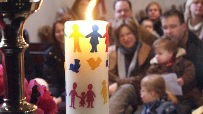 Leute sitzen in Kirche, Kerze mit Kinderbildern brennt