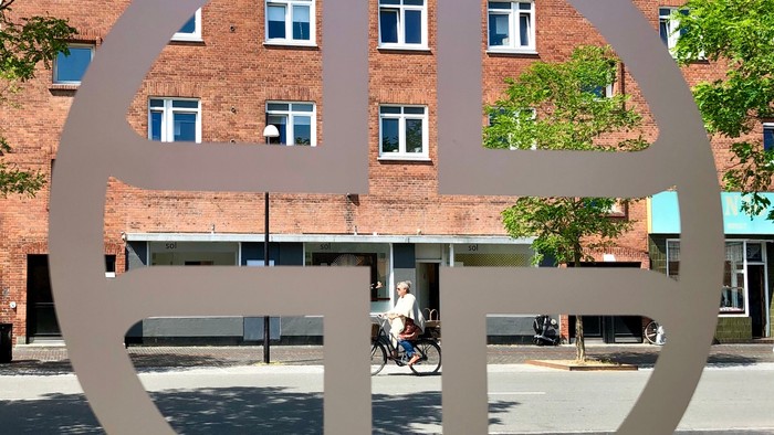 Stor, rund metalskulptur foran røde murstensbygning.