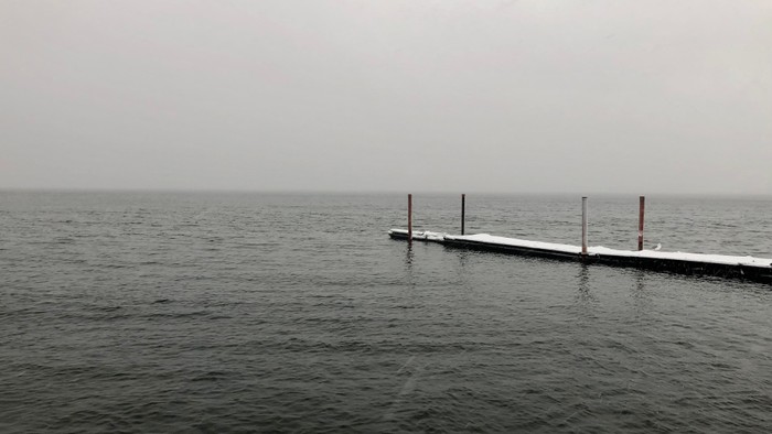 En lang kaj med to røde pæle udstikker sig i en trætt hav.