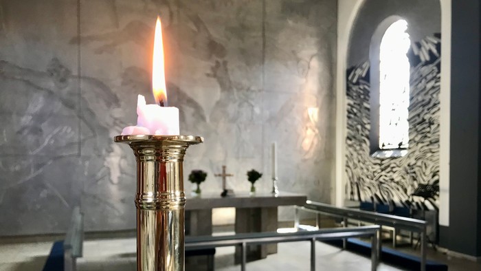 En lysende stearinlys i guldfarvet lysestage i kirke.