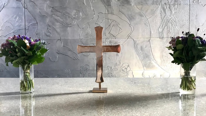 En altertavle med to blomsterstråer og et kors i forgrunden