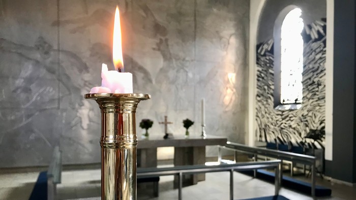 En lysende stearinlys i guldfarvet lysestage i kirke.