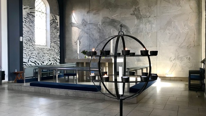 En moderne kirkeinterior med stor globus med lys og murmaleri.