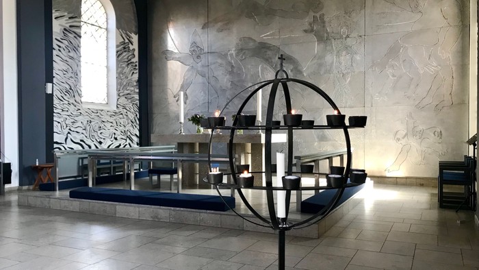 En moderne kirkeinterior med stor globus med lys og murmaleri.