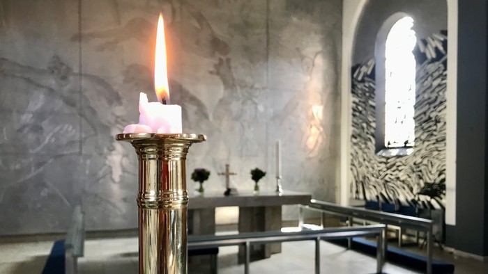 En lysende stearinlys i guldfarvet lysestage i kirke.