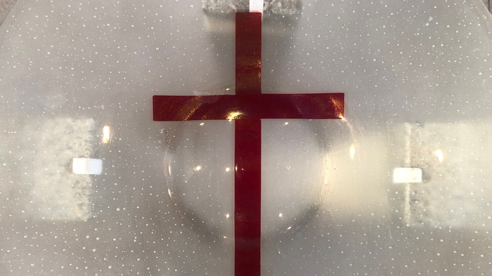 En rød kors monteret på en perforeret, reflekterende metaloverflade med en cirkulær lysrefleks.