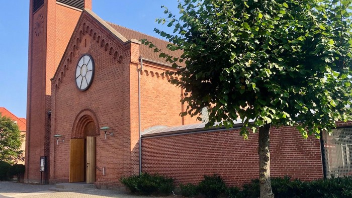 Røde murstenskirke med klokke og træ foran