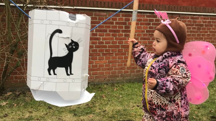 Et barn i kostume leger med en drage formet som en kat på et græsklædt område udendørs.