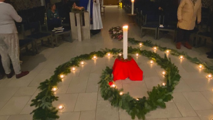 En gruppe mennesker i en kirke med en tændt lysestage og grønt foran.