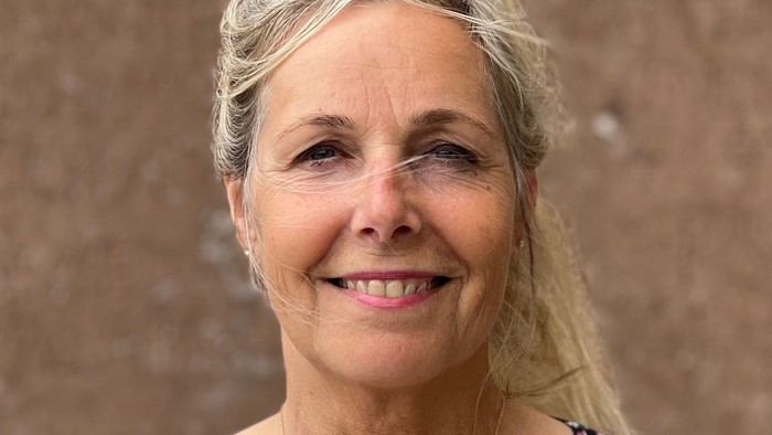 En kvinde med gråt hår, der bærer et korshalskæde og en blomstret top.