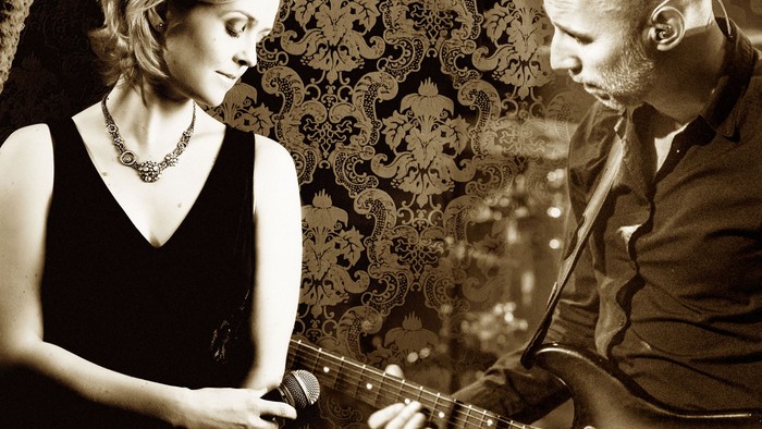 Ein Mann spielt Gitarre, während eine Frau in ein Mikrofon singt.