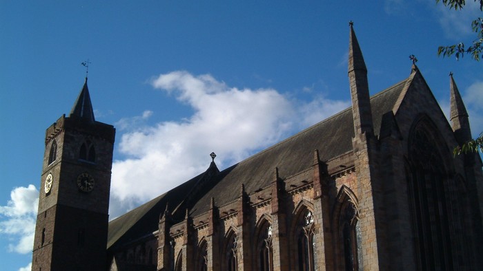 Large Gothic-style church with tall spires and clock tower against blue sky.