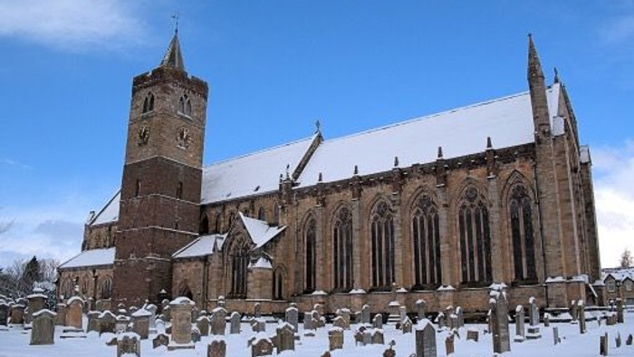 Historic snow-covered church with a tall bell tower and gravestones in a serene winter cemetery.