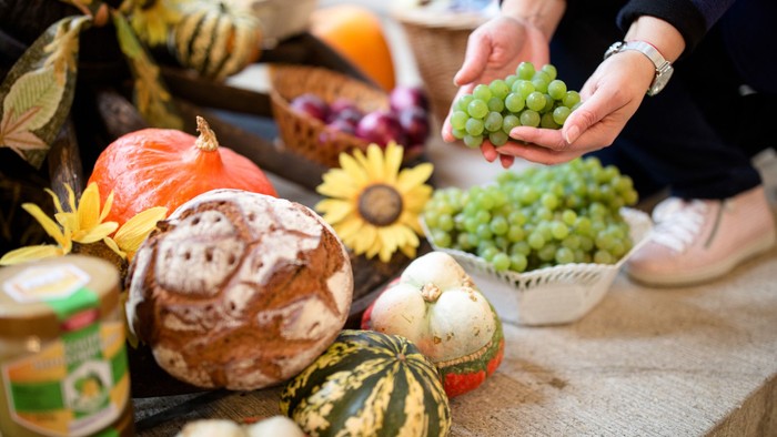 Eine Person hält eine Traube über einem Tisch mit verschiedenen Gemüsen und Blumen.