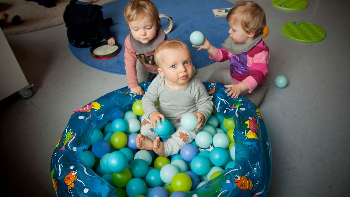 Tre små børn spiller i en ballespand med blå og grønne boller.