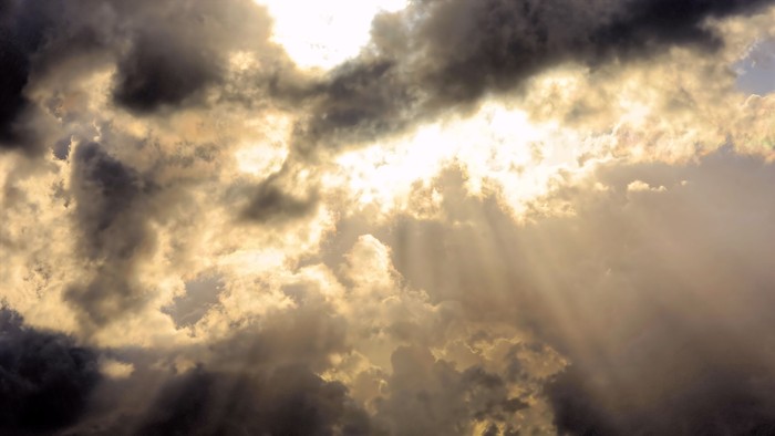 Skyen er fyldt med tætte, mørke skyer med solstråler, der skinner gennem dem.