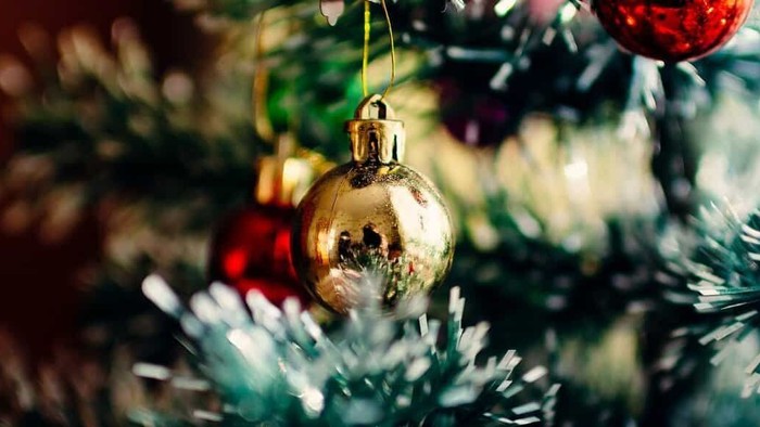 En juledekoreret træ med guldfarvede glaskugle og røde pynt.