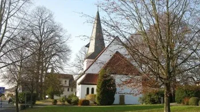 Kirchengelände mit weißem Kirchturm und rotem Dach, umgeben von Bäumen und Büschen
