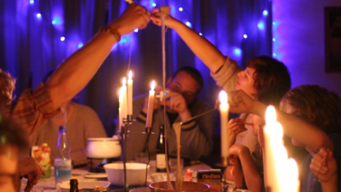 Eine Gruppe von Menschen feiert bei Kerzenschein und genießt ein Essen.