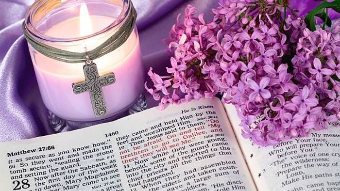 Lysestage med kors-charme ved siden af en åben bibel og lilla blomster