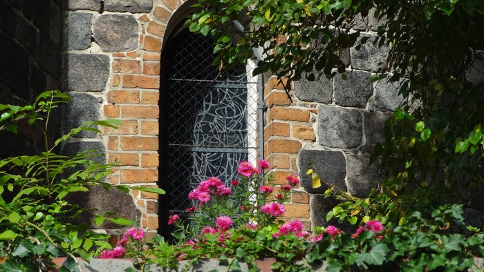 Ein Blumenbeet mit rosa Blumen vor einer Steingruppe mit Metalltür