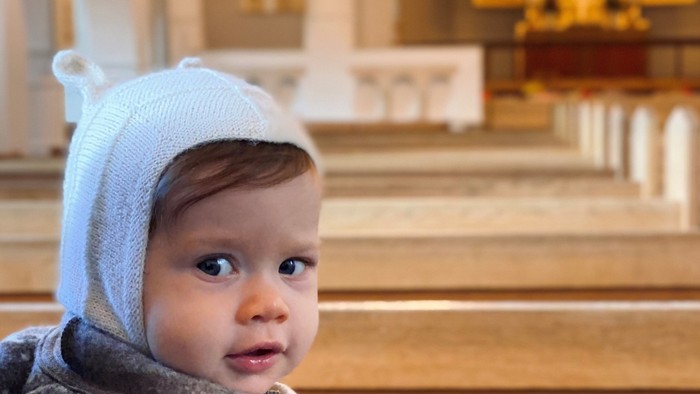 Børn med blå pude sitter i kirkebænke