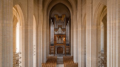 Indre del af en stor kirke med orgel og træbænke.