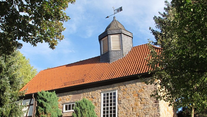 Steingebäude mit rotem Dach und Wetterhahn.