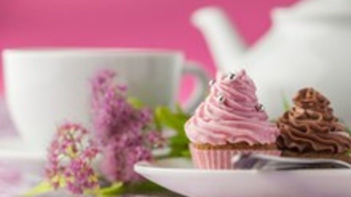 Delicious pink frosted cupcake and chocolate dessert on a plate with floral decor and teacup in background.
