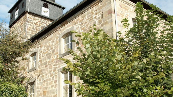 Steingebäude mit Turm und grünem Laub.